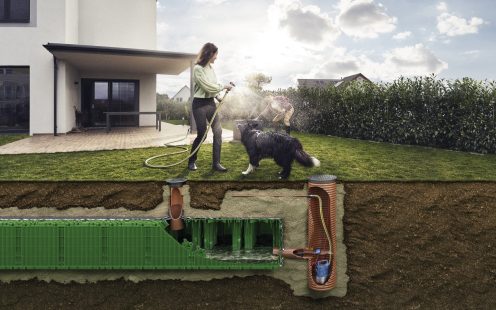 Egy nő a kertjében locsol egy kutya mellett, alattuk látszik egy esővíz szikkasztó rendszer a földben.